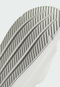 Semelle de chaussure avec une surface en caoutchouc blanc texturé, dotée de rainures et de crêtes horizontales pour une meilleure adhérence. Design à bord arrondi.