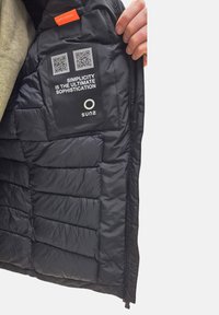 Interno della giacca nera isolata con sezioni imbottite, una toppa con codice QR e un'etichetta arancione "SAFE POCKET". Texture del tessuto liscia e lucida.