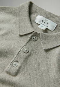 Polo shirt grigio chiaro realizzato in tessuto testurizzato. Presenta un colletto piegato e tre bottoni abbinati. L'etichetta riporta "THE SET, made in Bangladesh."