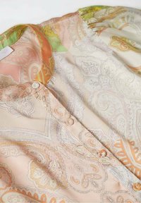 Blusa ligera y estampada de seda suave con intrincados diseños de paisley en tonos pastel de naranja, verde y crema, con cierres de botones.