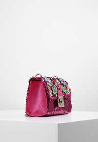 Vaaleanpunainen paljetein koristeltu käsilaukku, jossa on teksturoitu pinta, koristeltu läppä värikkäillä kivillä ja hopeinen lukon yksityiskohta. Kompakti, jäsennelty muoto.