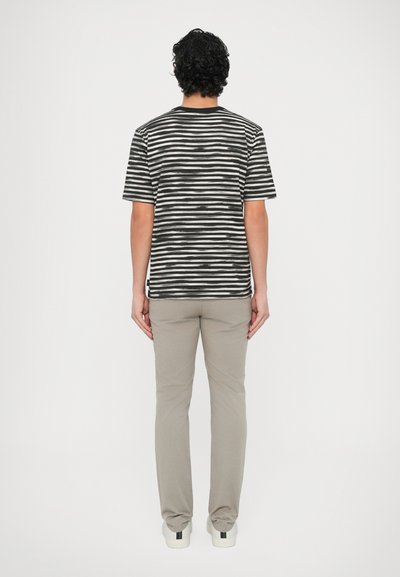 Svītrains T-krekls melnā un baltā krāsā, īsām piedurknēm, apaļu kakla izgriezumu; kombinēts ar gaiši bēšām biksēm un baltām kurpēm ar krāsainu akcentu.