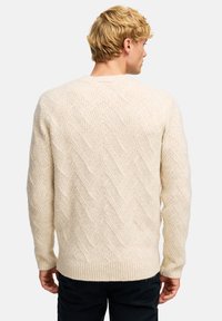 Sweter w kolorze kremowym, z dzianiny, o teksturowanym wzorze w jodełkę, z ściągaczami przy mankietach i u dołu, charakteryzujący się luźnym krojem i miękkim materiałem.