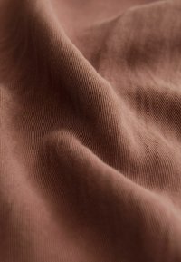 Material maro moale, încrețit, cu textură fină nervurată vertical și pliuri delicate care creează umbre și profunzime.