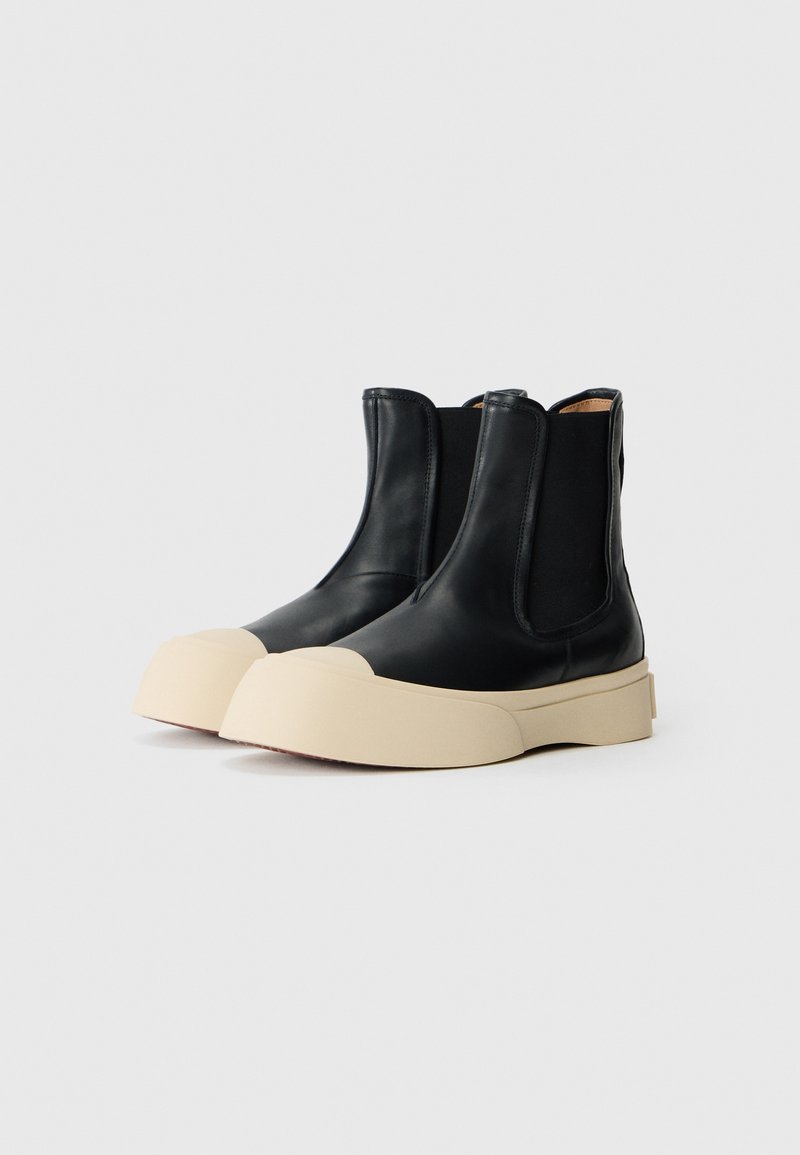 Stivaletti Chelsea neri in pelle con pannelli laterali elasticizzati, suole in gomma beige dalla forma arrotondata e una finitura liscia, caratterizzati da un design minimalista.