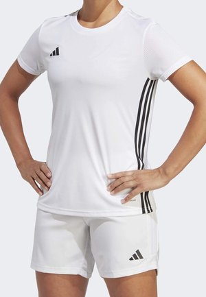 Person wearing a white Adidas sports outfit with black stripes on the sides, hands resting on hips, no head visible.
