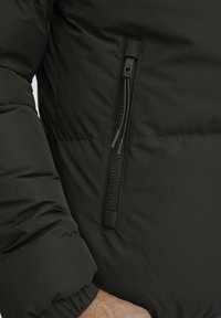 Svart pufferjakke med en glatt, matt finish. Har en glidel�åslomme på brystet og elastiske mansjetter for en tettsittende passform.