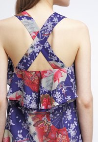 Snygg klänning utan axelband med korsade blommiga och koi-fisk mönstrade remmar över bar rygg, med lager av volanger.