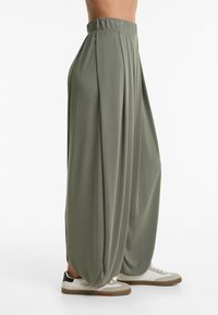 Pantaloni larghi di colore verde oliva con un design a gamba larga, vita elastica e texture morbida. Abbinati a sneakers bianche e beige.