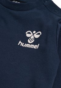 Mörkblå bomullsskjorta med rund hals, med vitt logotyp och grafisk design. Mjuk textur med tryckknappar på axeln.