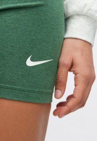 Πράσινο αθλητικό σορτς από απαλό ύφασμα, με λευκό λογότυπο Nike στην αριστερή πλευρά. Κοντινό πλάνο που δείχνει τις ραφές και τις λεπτομέρειες της υφής.