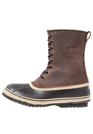 Botte d'hiver imperméable à lacets en cuir marron et caoutchouc noir avec semelle épaisse et logo Sorel embossé sur le côté.