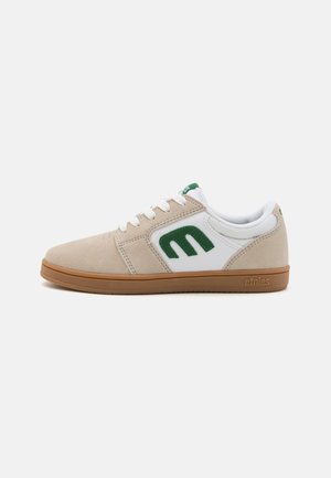 Baskets en nubuck beige et cuir blanc avec des accents verts. A des orteils ronds, un design à lacets, et une semelle en caoutchouc avec la marque "etnies".