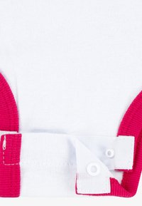 Λευκό βαμβακερό ενδύμα με ζωντανές ροζ ριμπ επενδύσεις και λευκή κλείστρο με κουμπιά στο πλάι, που αποκαλύπτει μαλακή υφή και ραμμένη λεπτομέρεια.