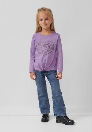 Lichtpaarse langemouwen shirt met een paardenafbeelding en tekst, geknoopt aan de onderkant, gecombineerd met blauwe spijker flared jeans en zwarte laarzen.