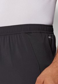 Sorte atletiske shorts har en elastisk talje, sidelommer og en glat tekstur, med et lille "DRY" logo på siden.