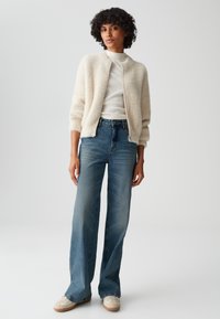 Cream fluffy bomber jacket over a light knit top, paired with high-waisted, wide-leg blue jeans and beige lace-up sneakers.