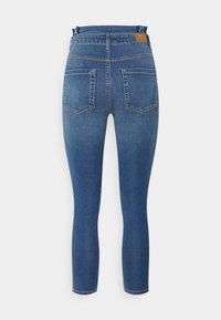 Calças skinny em denim azul escuro, com cintura alta, cinco bolsos e uma etiqueta de marca em couro castanho na parte de trás da cintura.