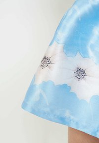 Tela de satén azul con un estampado floral que presenta grandes flores azules y pequeñas flores blancas. Textura suave y brillo delicado.