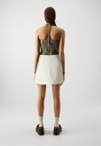 Haut sans bretelles avec un buste smocké vert et une mini jupe blanche ajustée avec des poches latérales et une fermeture éclair au dos. Des chaussures à plateforme marron complètent le look.