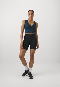 Tume teali värvi lühike tank top, mustad kõrge vöökohaga jalgrattapüksid, valged sokid mustade detailidega ja mustad spordijalatsid. Puhtad jooned ja hästi istuv disain.