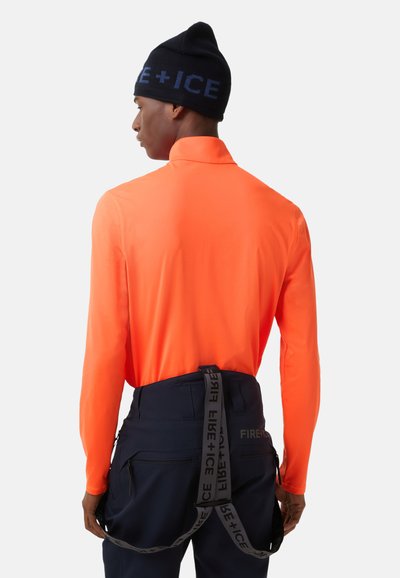 Koszula z długim rękawem w jaskrawym pomarańczowym kolorze, wykonana z lekkiego materiału, zestawiona z ciemnoniebieskimi spodniami z paskiem narzędziowym z logo.