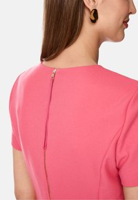 Rotes Kleid mit kurzen Ärmeln, einem hohen runden Ausschnitt und einem sichtbaren Reißverschluss auf der Rückseite, aus einem glatten Stoff.