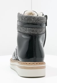 Svart lackläder ankelboot med grå ullkrage, vit vadderad sula och beige sömmar, visad bakifrån på vit yta.