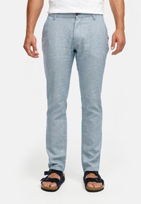 Lichtblauwe, slim-fit broek gemaakt van gestructureerde stof. Heeft vijf zakken en een knoopsluiting in de taille. Draagt bijpassende donkere sandalen.