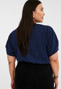 Mörkblå kortärmad blus med en texturerad leopardmönster, med rund halsringning och avslappnad passform, matchad med svarta jeans.