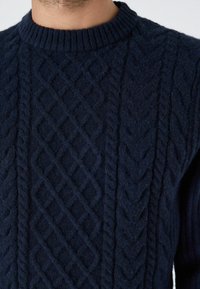 Marineblauer Strickpullover mit einem strukturierten Kabelmuster, ausgestattet mit einem gerippten Rundhalsausschnitt und aus weichem Wollmaterial.