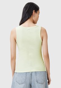 Top sin mangas de color verde claro, hecho de algodón suave, con un cuello redondo y una silueta ajustada, con una pequeña etiqueta de logo en la parte posterior.