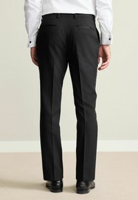 Schwarze maßgeschneiderte Hose aus glattem Stoff, ausgestattet mit zwei Gesäßtaschen, geraden Beinen und einem eleganten Finish, kombiniert mit glänzenden schwarzen Schuhen.