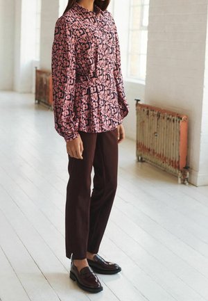Blouse à motifs rose et marine avec un col et une texture plissée, associée à un pantalon slim bordeaux et des mocassins foncés brillants.