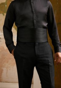 Conjunto negro a medida que incluye una camisa de manga larga con botones en la parte delantera y una cinturilla ancha y suave, combinada con pantalones negros texturizados.