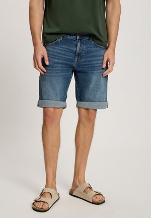 Blaue Denim-Shorts mit umgeschlagenen Säumen, ausgestattet mit einem klassischen Fünf-Taschen-Design, kombiniert mit beigen Schiebesandalen. Strukturierter Stoff.