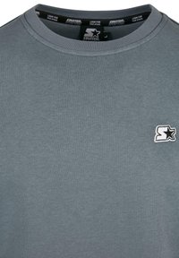 Felpa grigia con scollo rotondo in cotone. Presenta un piccolo logo bianco ricamato sul petto. Texture liscia con polsini e collo a costine.