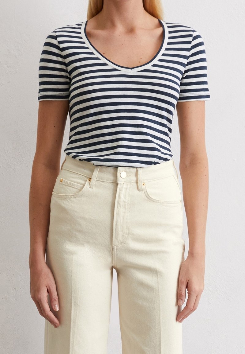 Marineblå og hvide stribede kortærmede T-shirt med V-hals. Kombineret med høj talje lyscremefarvede denimjeans med knaplukning.