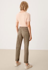 T-shirt rosa chiaro a maniche corte abbinato a pantaloni verde oliva, dotati di due tasche posteriori e risvolti, indossato con sneakers beige.