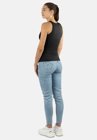 Schwarz ärmelloses Top, kombiniert mit hellblauen Jeans und weißen Sneakern. Das Top ist enganliegend, und die Jeans sind schmal geschnitten im klassischen Fünf-Taschen-Design.