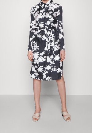 Black and white floral patterned long-sleeve shirt dress with waist tie, worn with beige open-toe crisscross mule heels.