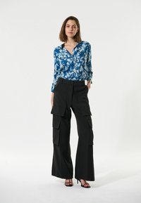 Blaue Blumen-Hemd mit Knöpfen, kombiniert mit hochtaillierten schwarzen Cargo-Hosen mit Taschen. Das Outfit hat eine lässige Passform und ein vielseitiges Design.