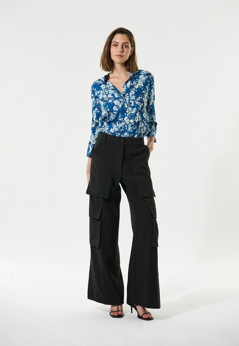 Blaue Blumen-Hemd mit Knöpfen, kombiniert mit hochtaillierten schwarzen Cargo-Hosen mit Taschen. Das Outfit hat eine lässige Passform und ein vielseitiges Design.