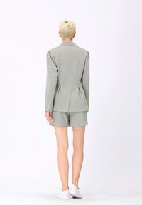 Blazer à carreaux gris avec une coupe ajustée, associé à un short assorti. Le blazer présente de subtils épaulettes et des boutons dorés.