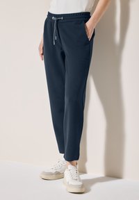 Mörkblå sweatpants med strukturerad yta, elastisk midja, dragsko och sidofickor, matchade med vita sneakers.