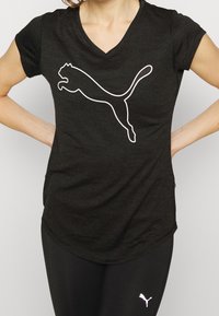 Svart v-ringad t-shirt i mjukt tyg med en vit hoppande puma-logotyp. Bärs med svarta leggings, vilket visar en sportig design.