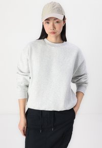Grijze sweatshirt met een ronde hals en geribbelde manchetten, gedragen met een beige pet met een logopatch, en gecombineerd met donkere broeken.