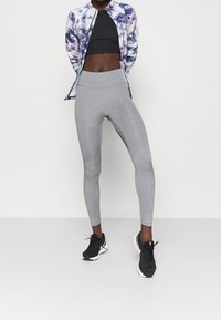 Conjunto deportivo que presenta una chaqueta con cremallera de estampado en tonos púrpura y azul, top corto negro, mallas grises y zapatillas deportivas negras.