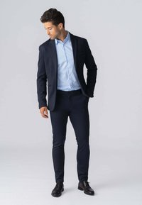 Marineblå jakkesætjakke over en lyseblå stribet skjorte, slim-fit marineblå bukser og mørkebrune sko, der skaber et koordineret formelt outfit.