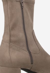 Bottine en suède beige avec un talon empilé, dotée d'une fermeture éclair latérale et de coutures invisibles pour un design épuré.